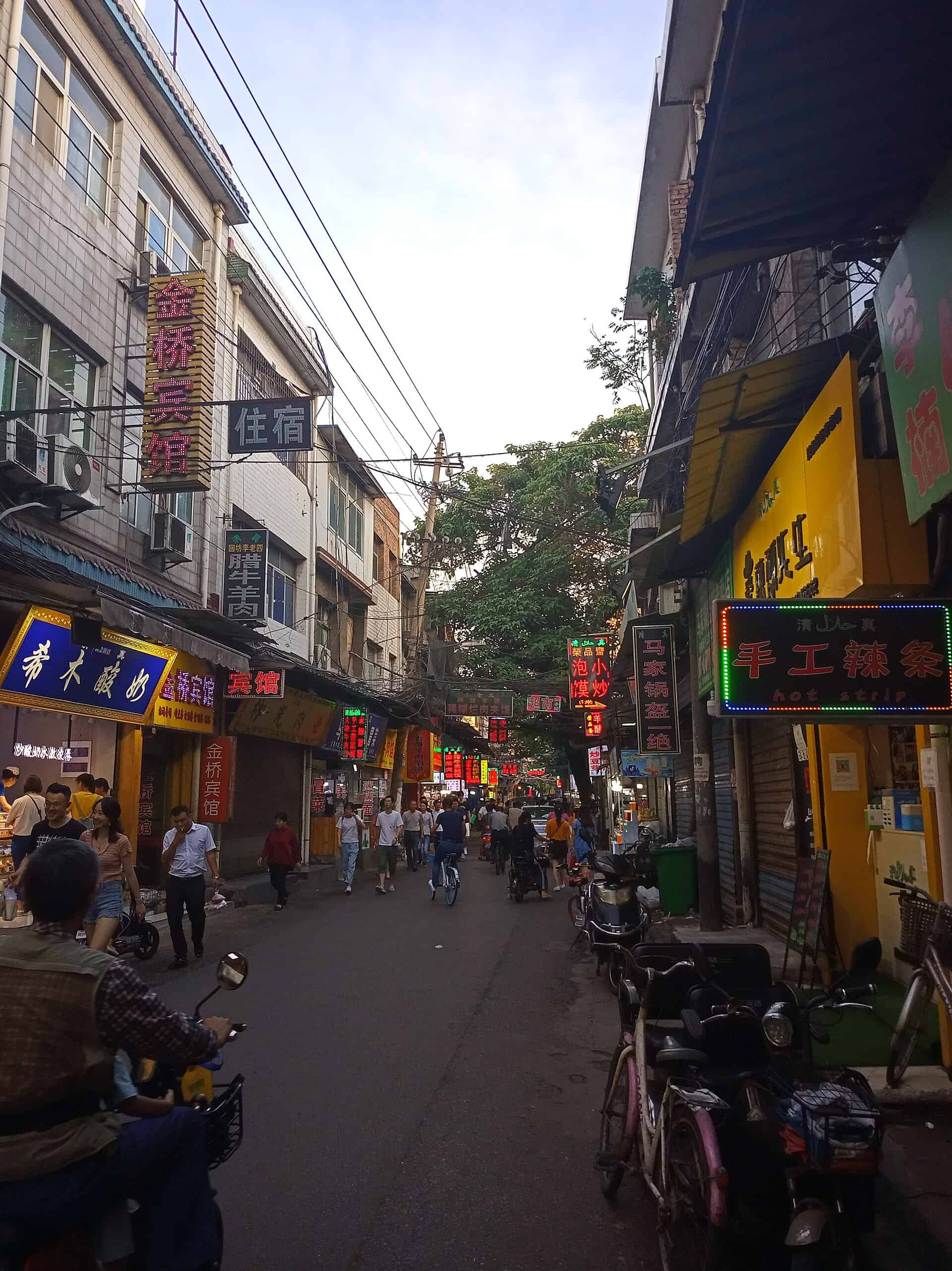 Sajinqiao food street at dusk — halal snack stalls and glowing neon signs in Xi'an's Lianhu district