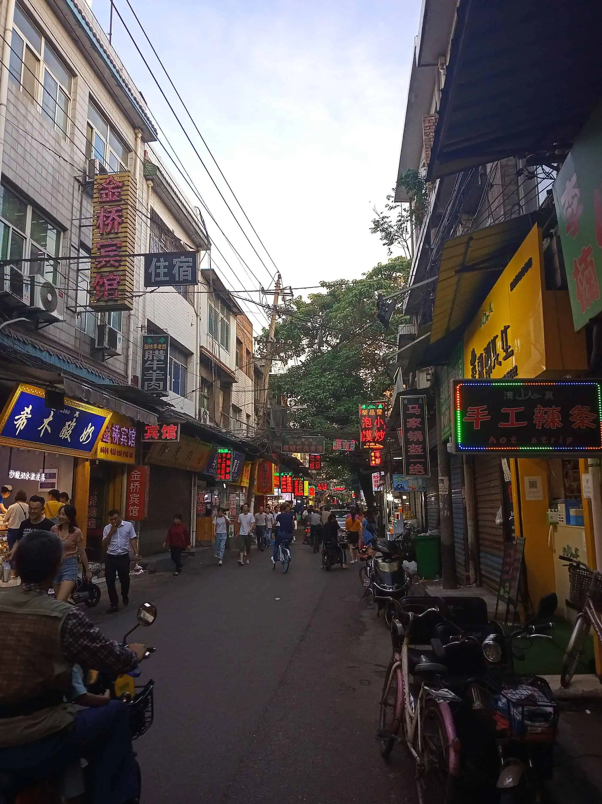 Sajinqiao food street at dusk — halal snack stalls and glowing neon signs in Xi'an's Lianhu district